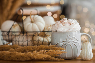 Delicious pumpkin latte with whipped cream and cinnamon in a mug on the table in the living room interior. Autumn decor in the house. Scandinavian style.