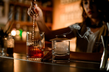 Focus on two glasses on the bar counter, in one of which a female bartender is stirring a cocktail