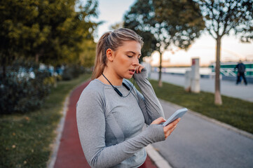 Woman adjusting headphones and using fitness app on smartphone after running