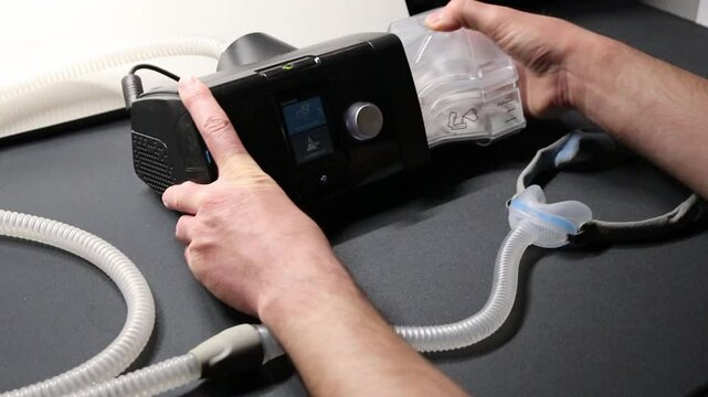 Male European with cpap machine checking therapy equipment like cpap filter or humidifier for health check and night preparation for innovative healthy sleep respiratory system with sleep apnea mask