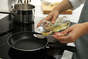 Woman with bottle of oil and spoon in kitchen, closeup