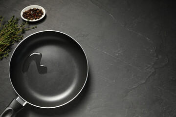 Frying pan with oil and spices on dark gray textured table, flat lay. Space for text