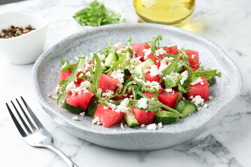 Delicious watermelon salad with feta cheese, cucumber and arugula served on white marble table, closeup