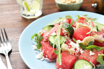 Tasty salad with watermelon, feta cheese, cashews and arugula on wooden table, closeup