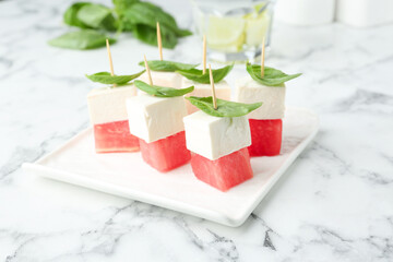Tasty canapes with watermelon, feta cheese and basil on white marble table