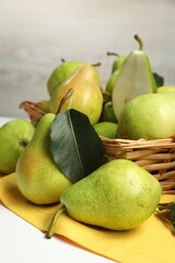Fresh green pears with leaves and basket on white table, closeup