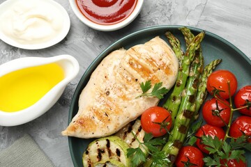 Delicious grilled vegetables and chicken breast served on grey textured table, flat lay