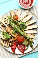Delicious grilled vegetables and cut chicken meat served with sauce on light blue wooden table, flat lay