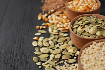 Different types of seeds and cereals in bowls on black wooden table, closeup. Space for text