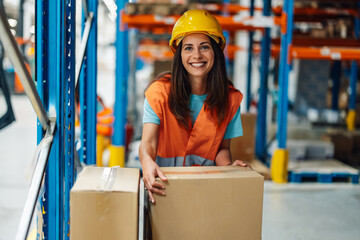 Female warehouse worker smiling and lifting box in a storage room