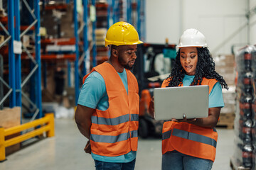 Warehouse workers using laptop discussing logistics and inventory management