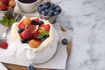 Pavlova cake (meringue dessert) with whipped cream, fresh berries, fig and mint on white marble table, closeup