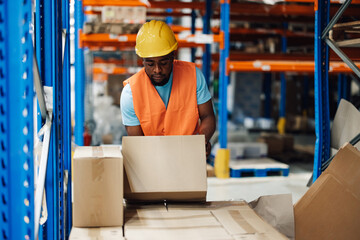 Warehouse worker picking up cardboard box from shelf