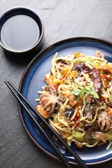 Stir-fry noodles with sea food, vegetables and soy sauce on dark textured table, top view