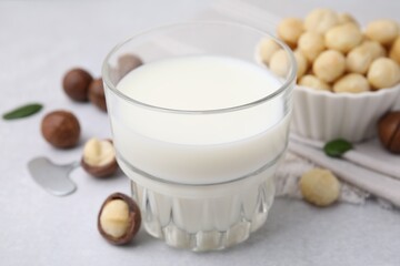 Glass of macadamia milk and nuts on white table, closeup
