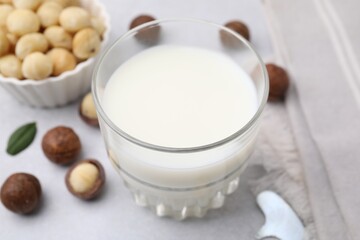 Glass of macadamia milk and nuts on white table, closeup