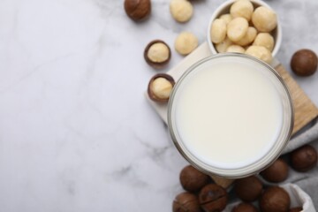 Glass of macadamia milk and nuts on white marble table, flat lay. Space for text