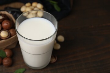 Glass of macadamia milk and nuts on wooden table, closeup. Space for text