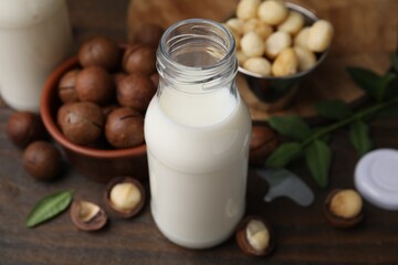 Bottle of macadamia milk and nuts on wooden table, closeup
