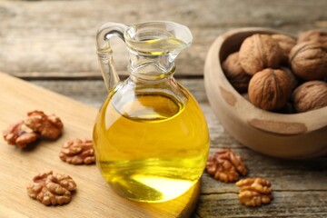 Cooking oil in jug and walnuts on wooden table, closeup