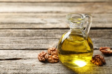 Cooking oil in jug and walnuts on wooden table, closeup. Space for text