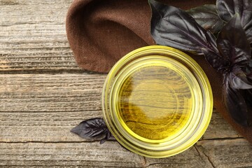 Cooking oil in bowl and red basil on wooden table, top view. Space for text