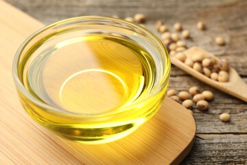 Cooking oil in bowl and soybeans on wooden table, closeup