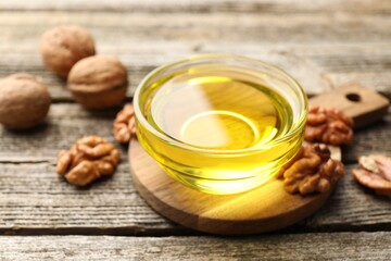 Cooking oil in bowl and walnuts on wooden table, closeup