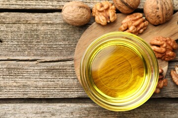 Cooking oil in bowl and walnuts on wooden table, top view. Space for text