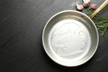 Frying pan with cooking oil, rosemary, garlic and salt on dark textured table, flat lay. Space for text