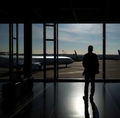 Fototapeta premium Silhouette of a man standing at the airport and looks towards a large window through which a plane is visible