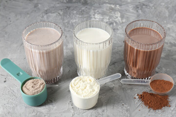 Delicious protein shakes in glasses and scoops with powder on gray textured table, closeup