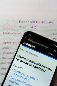 UK government website on mobile device next to DBS Enhanced certificate for checking someone's criminal record online. Stafford, United Kingdom, August 7, 2024..