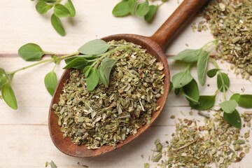 Dried oregano in spoon and green leaves on wooden table, closeup