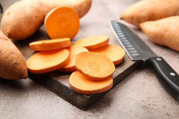 Fresh raw sweet potatoes and knife on gray textured table, closeup