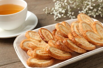 Tasty french palmier cookies, tea and gypsophila flowers on wooden table, closeup