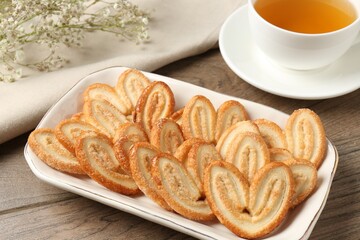 Tasty french palmier cookies, tea and gypsophila flowers on wooden table, closeup