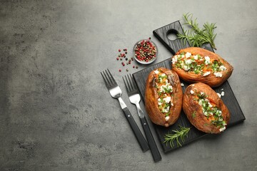 Tasty cooked sweet potatoes with feta cheese, green onion and parsley served on gray textured table, flat lay. Space for text