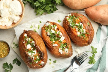 Tasty cooked sweet potatoes with feta cheese, green onion and parsley served on gray textured table, flat lay