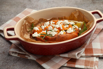 Tasty baked sweet potato with feta cheese and herbs on grey textured table, closeup