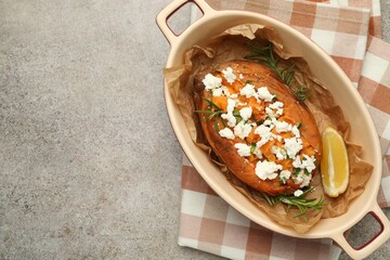 Tasty baked sweet potato with feta cheese, lemon and herbs on grey textured table, top view. Space for text