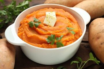 Tasty mashed sweet potato with butter in bowl, fresh vegetables and parsley on table, closeup