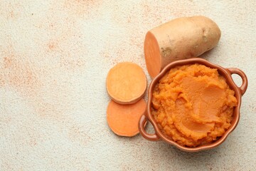 Tasty mashed sweet potato in bowl and cut vegetable on beige textured table, flat lay. Space for text