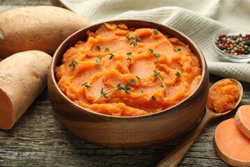 Tasty mashed sweet potato with thyme in bowl and fresh vegetables on wooden table, closeup