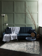 Cozy living room arrangement featuring a green wall, dark blue sofa with a blanket, and minimalist decor in soft lighting