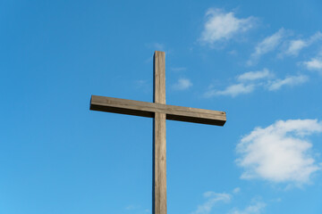 An Orthodox wooden cross on a background of blue sky and clouds. An old antique cross close-up.