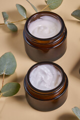 Set of moisturizer cream jar in amber glass bottles and dry eucalyptus on beige background. Set for skin and body care beauty products