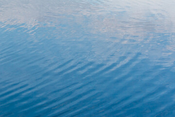 Close up photo of waves ripples on blue water surface spreading. Blurred defocus shining water surface background.
