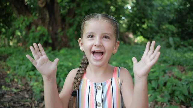 Girl cheers clapping her hands outdoors with green nature