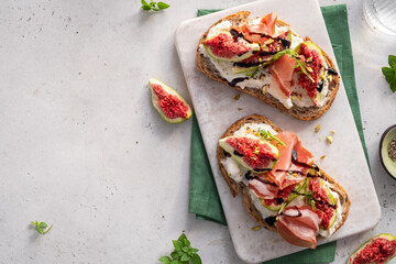 Two slices of bread with figs and ham on top of a white plate